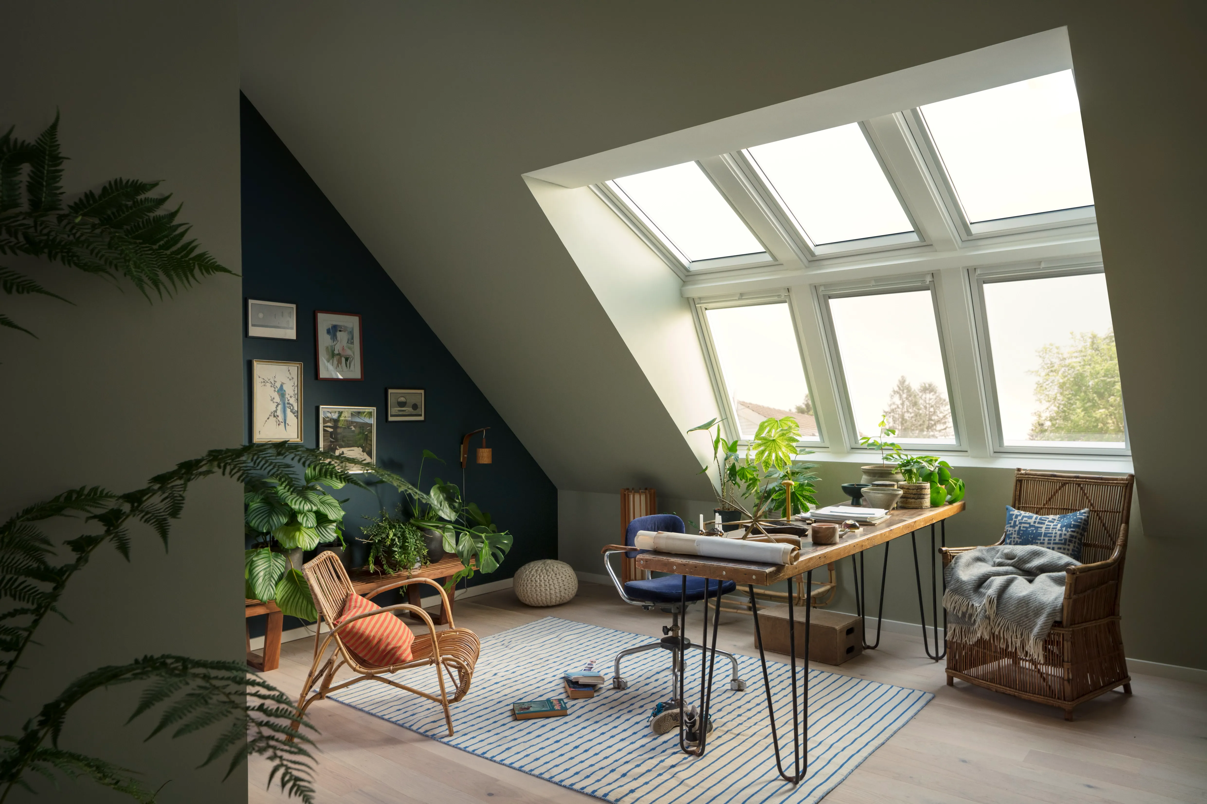 A room with a desk, chair, potted plants and a window.